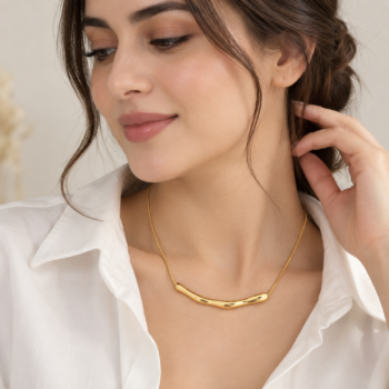 Model wearing organic curved gold bar necklace centered along collarbone with open collar